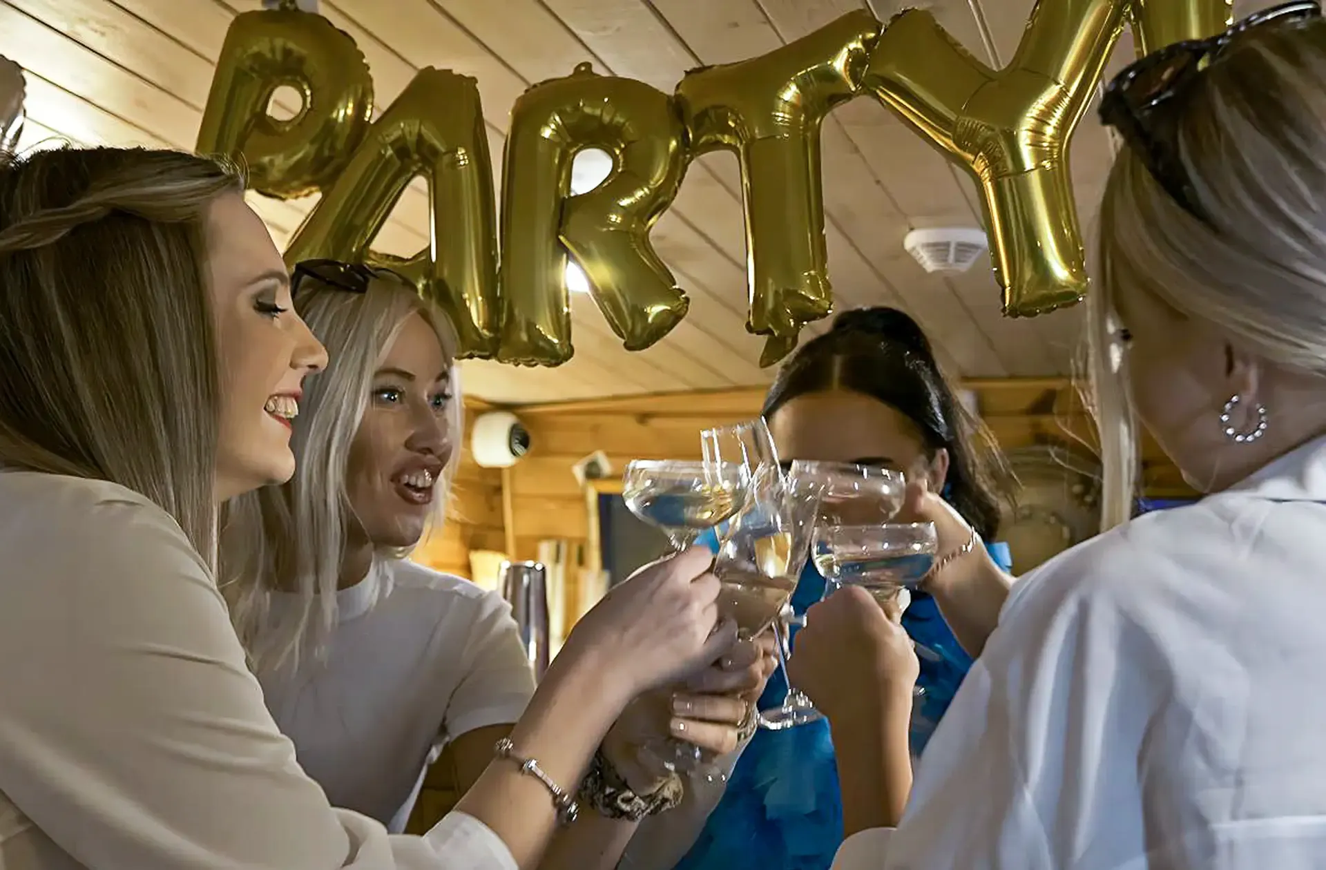 Friends raising a toast under gold PARTY balloons in the cabin