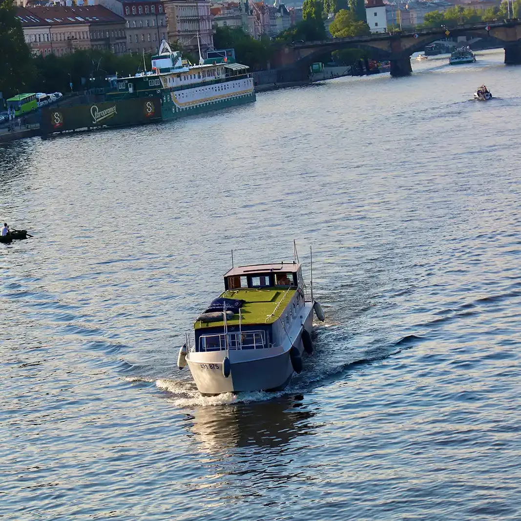 Loď Imago Mundi se zelenou střechou pluje po Vltavě, v pozadí Praha