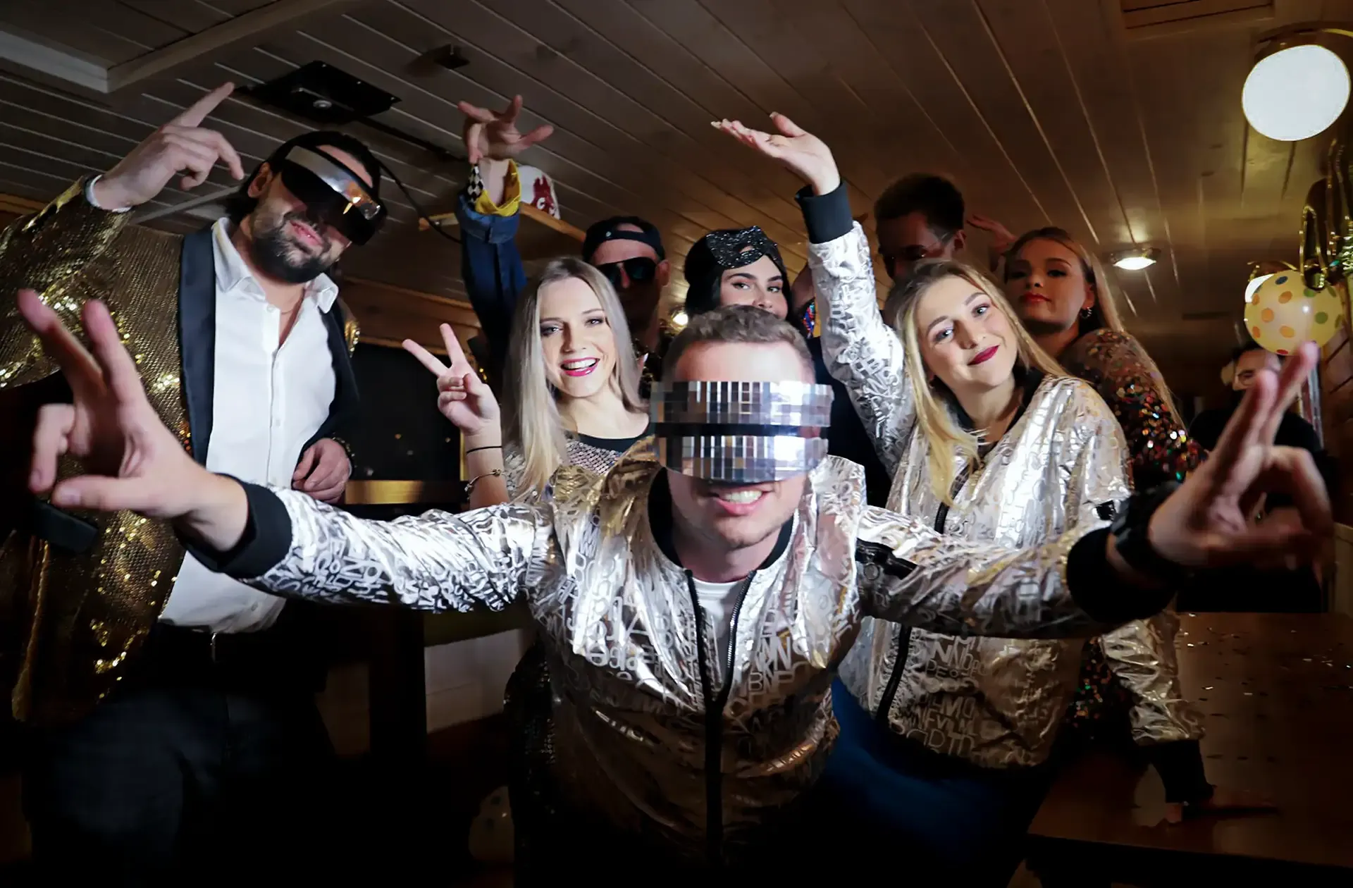 Party guests in shiny silver jackets and futuristic glasses posing in the cabin of Imago Mundi