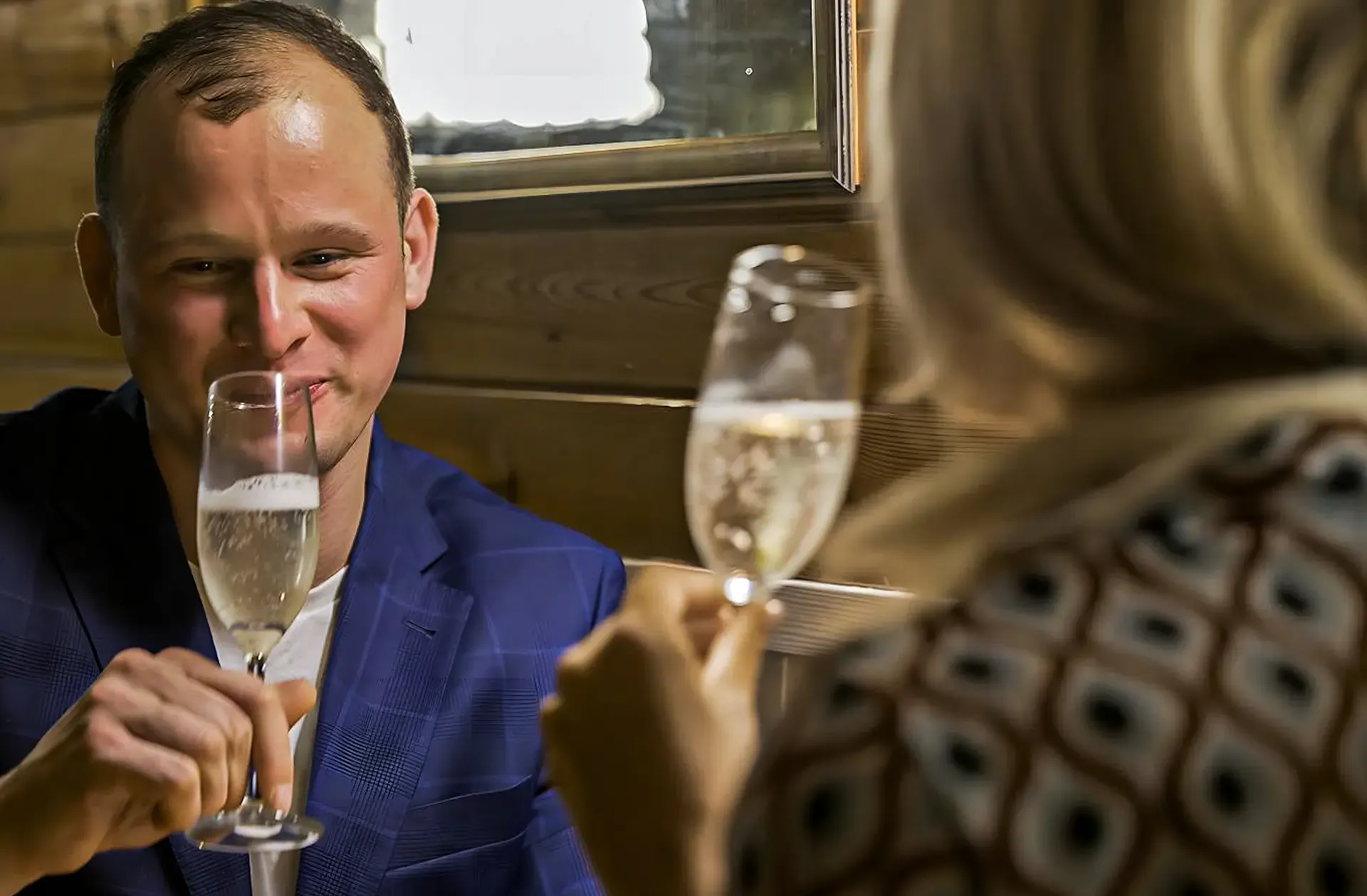 Muž v modrém saku si připíjí sektem s partnerkou v salonu lodi