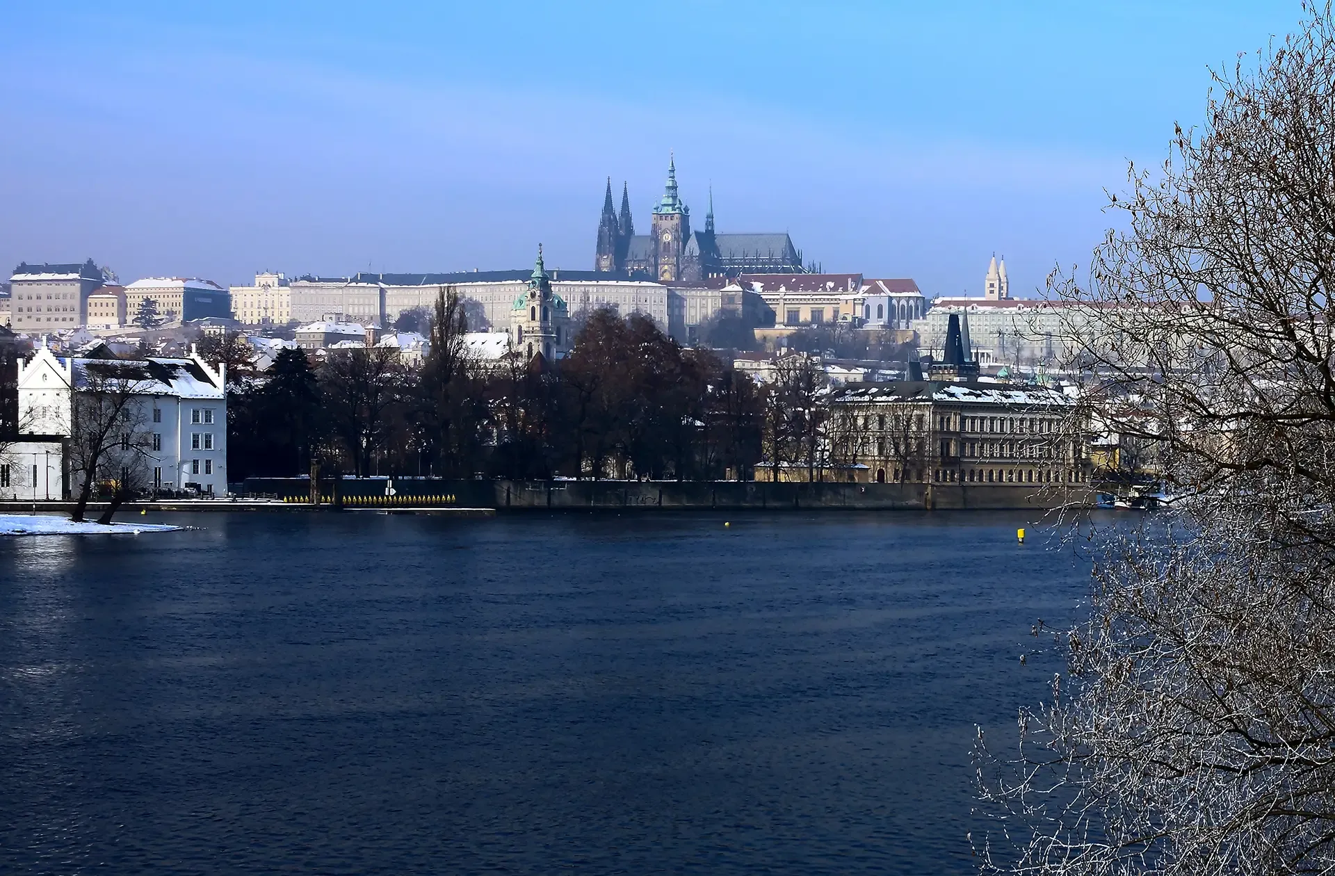 Zasněžený Pražský hrad nad Vltavou za zimního dne